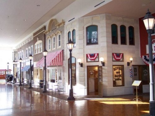 A charming indoor street scene with storefronts, decorative awnings, and vintage-style street lamps.
