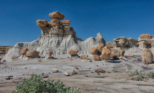 A unique rock formation with large boulders atop a sandy landscape under a clear blue sky.