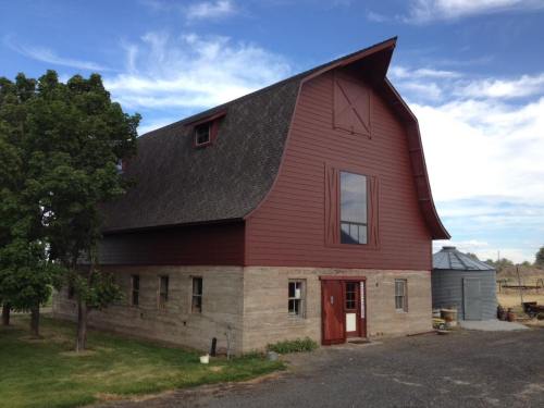 A large red barn with a sloped roof, surrounded by green grass and trees under a blue sky with clouds.