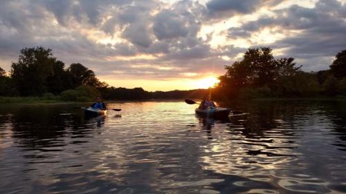 Two people kayaking on a calm river at sunset, with vibrant clouds reflecting on the water.