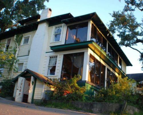 A charming two-story house with large windows, surrounded by greenery, featuring a sign that reads "Julep."