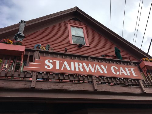 A red building with a sign reading "Stairway Cafe" and flower pots on the balcony.