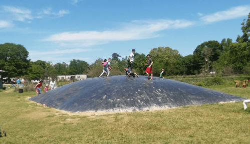 Children playing on a large, black, inflatable dome in a grassy field under a clear blue sky.