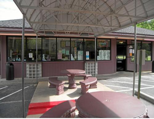 A small food stand with a covered outdoor seating area and a menu displayed in the window.