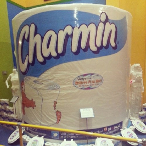 Giant Charmin toilet paper roll display at a museum, surrounded by smaller toilet paper sculptures.