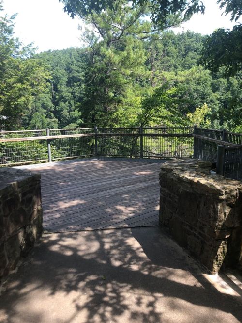 A wooden viewing platform surrounded by trees, overlooking a lush green landscape.