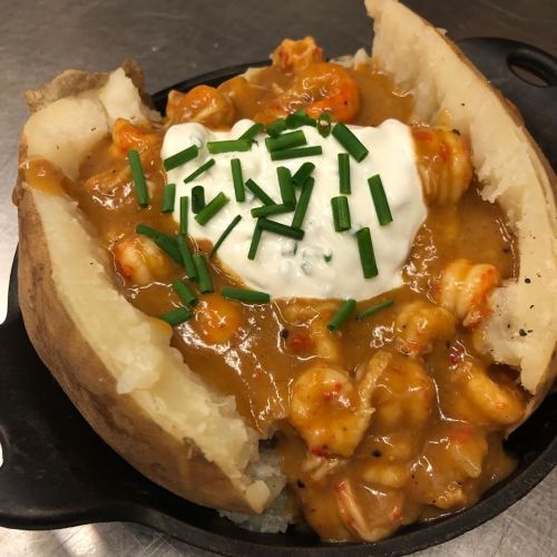 Baked potato topped with shrimp sauce, sour cream, and chives, served in a small cast iron skillet.