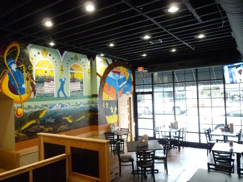 A vibrant restaurant interior featuring colorful murals, wooden tables, and large windows letting in natural light.
