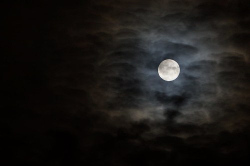 A bright full moon surrounded by dark, swirling clouds in a night sky.