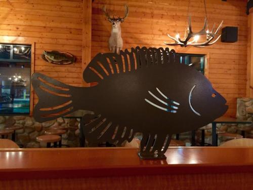 A metal fish sculpture on a wooden counter, with a rustic restaurant interior featuring deer antlers and stone walls.