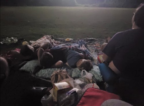 A group of people sleeping on blankets outdoors at night, with some snacks scattered around.