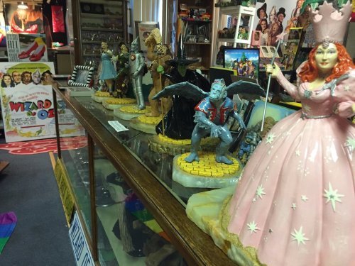 A display of colorful figurines from "The Wizard of Oz" in a vintage shop, featuring characters like Glinda and the Tin Man.