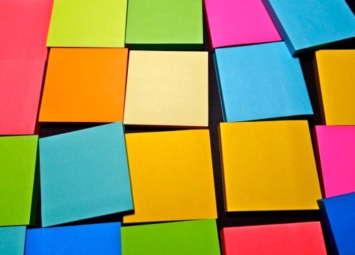 A colorful arrangement of sticky notes in various shades of pink, orange, yellow, green, and blue on a dark background.