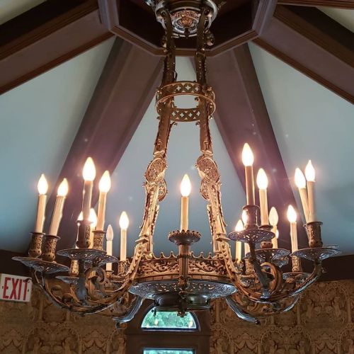 A decorative chandelier with multiple candle-like lights, hanging from a vaulted ceiling in an elegant room.