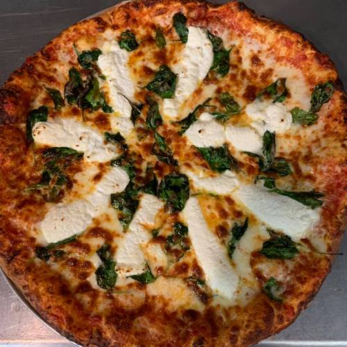 A freshly baked pizza topped with cheese, spinach, and dollops of ricotta, on a metal tray.