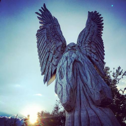 A large wooden angel statue with outstretched wings against a sunset sky.