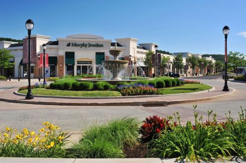A vibrant shopping plaza featuring a central fountain surrounded by colorful flowers and greenery.