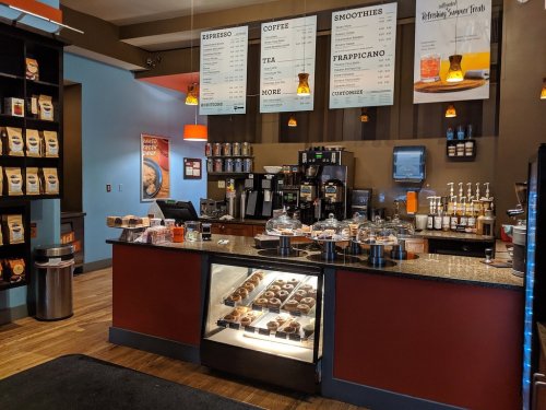 A cozy café counter with a display of pastries, coffee machines, and a menu board featuring drinks and snacks.