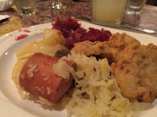 A plate of food featuring fried chicken, sauerkraut, sausage, potatoes, and red cabbage.