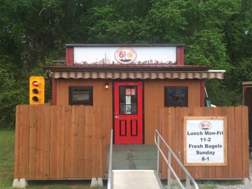A small wooden building with a red door, serving bagels, surrounded by greenery and a traffic light nearby.