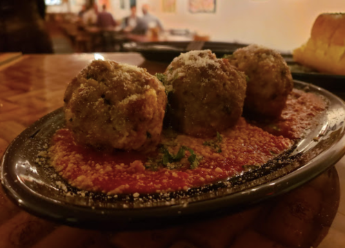 Three meatballs on a plate with marinara sauce, sprinkled with cheese and herbs, set in a cozy restaurant ambiance.
