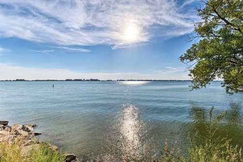 A serene lake scene with calm water reflecting the sun and a clear blue sky, framed by greenery on the shore.