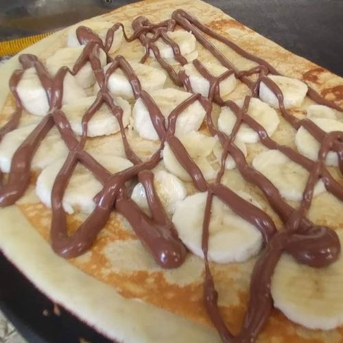 A close-up of a crepe topped with sliced bananas and drizzled with chocolate sauce.