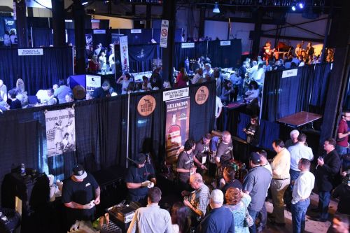 A bustling event with vendors and attendees, featuring booths, food, and drinks in a large indoor space.