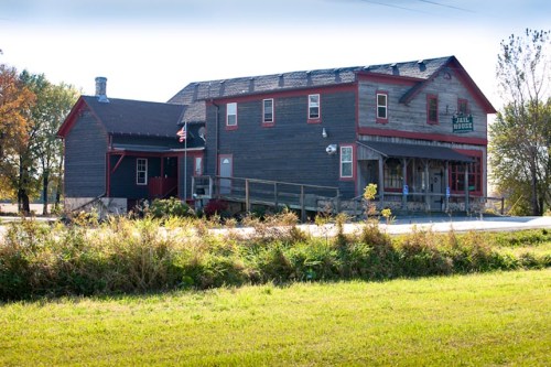 A rustic two-story building with a wooden exterior, red accents, and a porch, set against a clear blue sky.