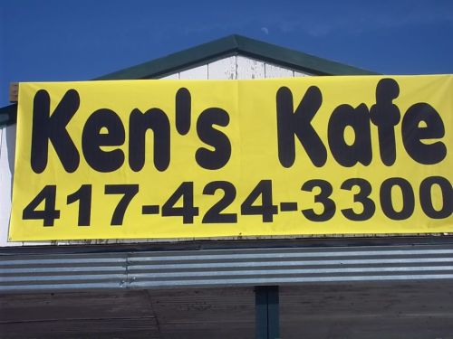 Sign for Ken's Kafe with a yellow background and bold black text displaying the name and phone number.