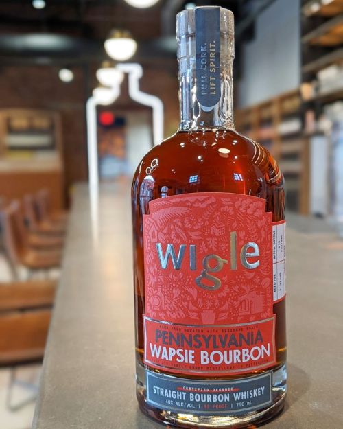 A bottle of Wigle Pennsylvania Wapsie Bourbon whiskey on a bar counter, featuring a vibrant red label.
