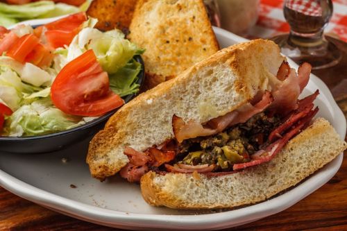 A hearty sandwich with layers of meat, served with a side salad and toasted bread on a plate.