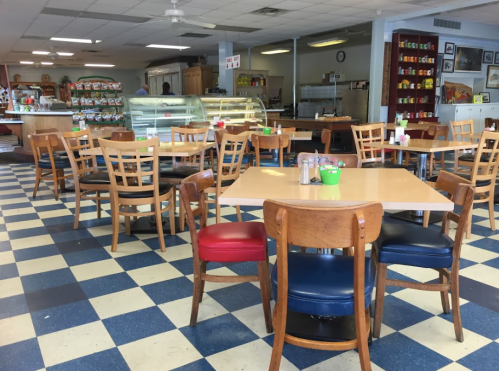 A cozy diner with wooden tables and chairs, featuring a checkered floor and a display case in the background.