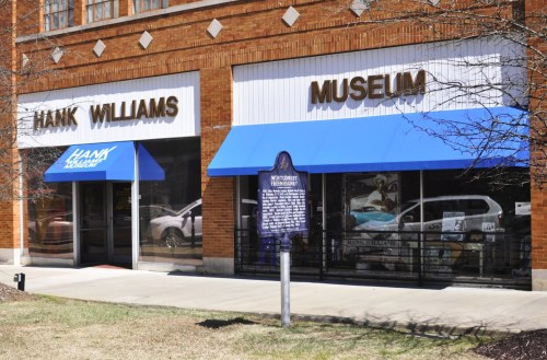 Exterior of the Hank Williams Museum, featuring blue awnings and a historical marker in front.