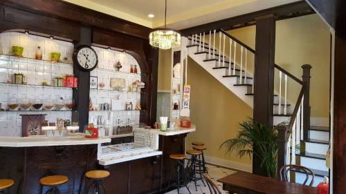 Cozy café interior featuring a bar with a clock, decorative shelves, and a staircase in a warm, inviting atmosphere.