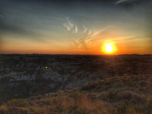 Sunset over rugged hills, with vibrant orange and yellow hues illuminating the sky and landscape.