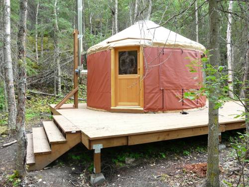 A wooden yurt on a raised deck, surrounded by trees in a forested area.