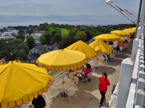 A scenic outdoor dining area with yellow umbrellas, overlooking a lush landscape and a body of water.