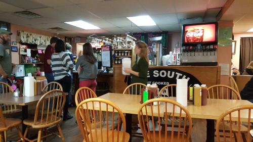 A cozy restaurant interior with wooden tables, patrons at the counter, and a soda machine in the background.