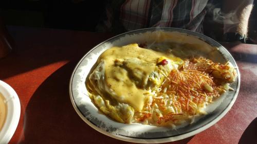 A plate of cheesy omelette with hash browns, served hot on a table with sunlight streaming in.