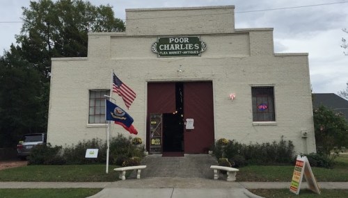 Exterior of Poor Charlie's flea market and antiques store, featuring an American flag and a Louisiana state flag.