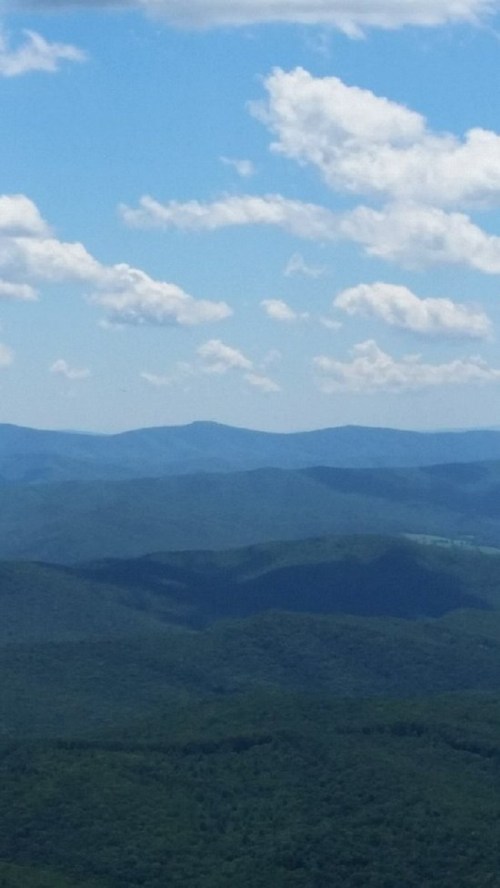 A panoramic view of rolling green mountains under a blue sky with fluffy white clouds.