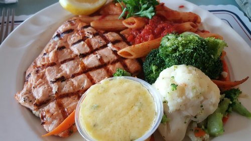 Grilled salmon with lemon, pasta in marinara, broccoli, and mashed vegetables on a white plate.