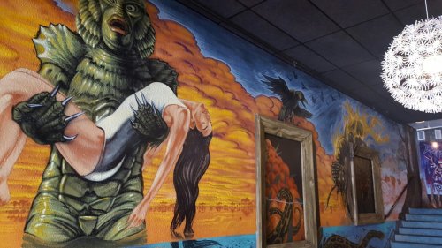A vibrant mural depicting a creature holding a woman against a dramatic, colorful sky backdrop.