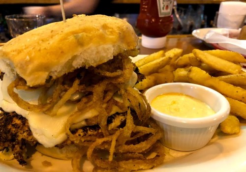 A close-up of a chicken sandwich topped with fried onions, served with a side of fries and a small cup of dipping sauce.