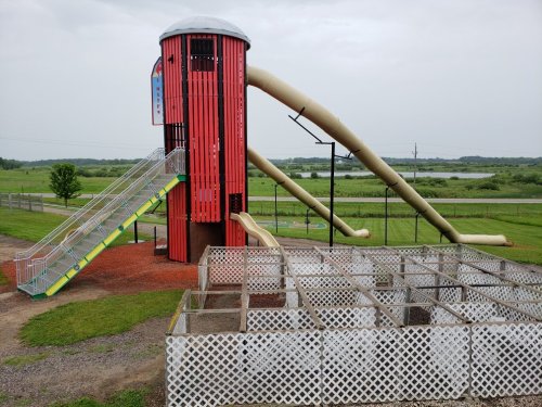 A colorful playground featuring a tall slide tower and a winding slide, surrounded by a fenced play area.