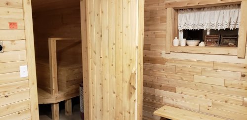 A wooden interior featuring a sauna door, a window with lace curtains, and a wooden bench.