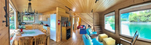Cozy wooden interior of a cabin with a kitchen, dining area, and living space overlooking a serene lake.