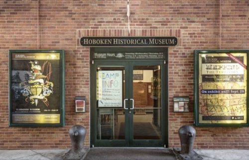 Entrance of the Hoboken Historical Museum, featuring brick walls and informational posters on either side.