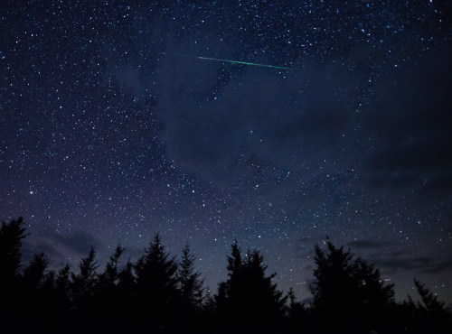 A starry night sky filled with twinkling stars and a bright meteor streaking across the dark backdrop.